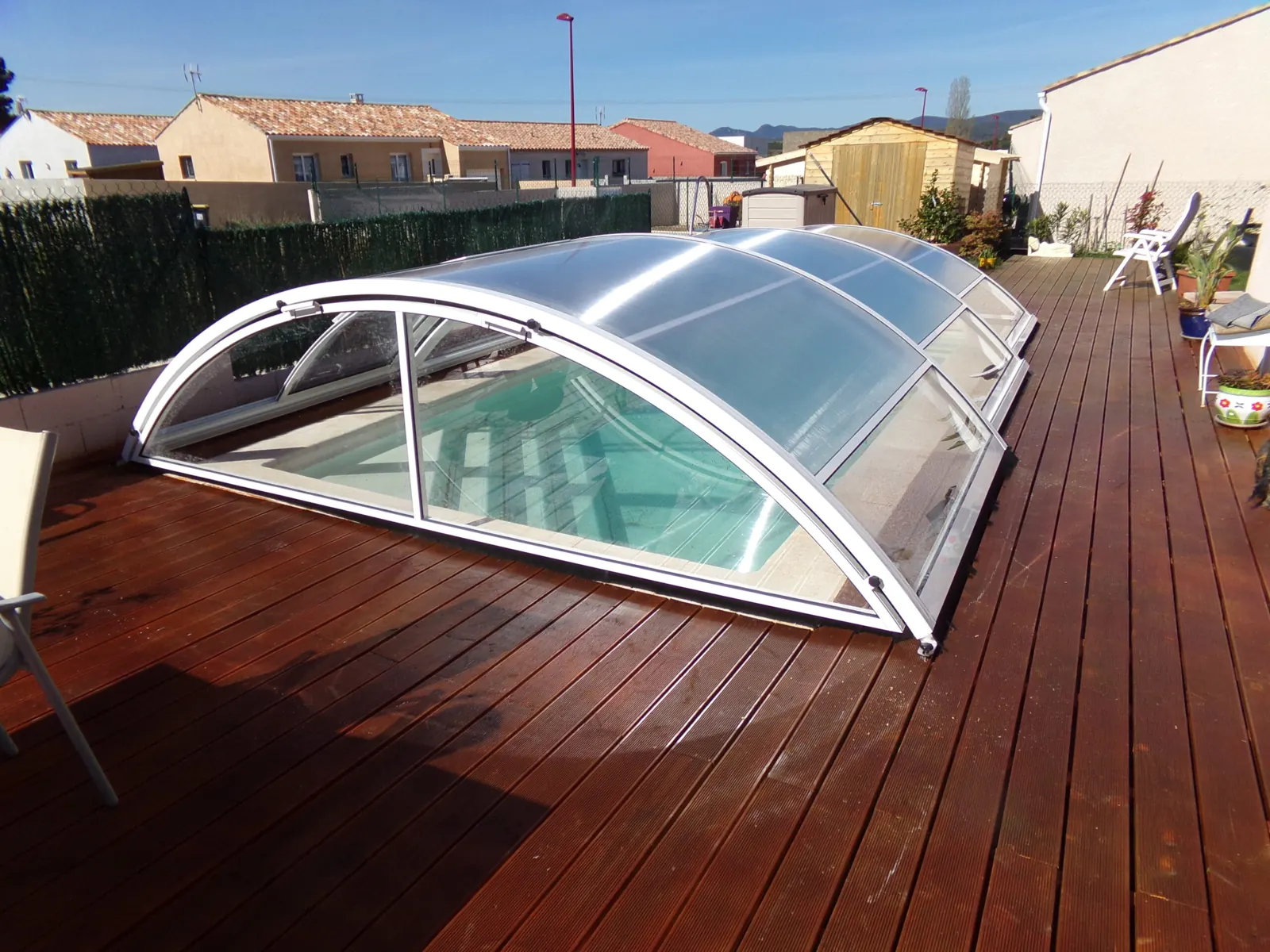 Abri de piscine bas à arceaux blancs posé sur un deck en bois exotique
