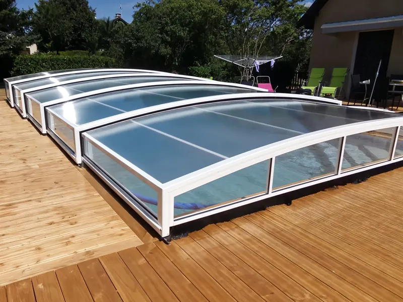 Abri de piscine bas à arceaux blancs posé sur une terrasse en bois