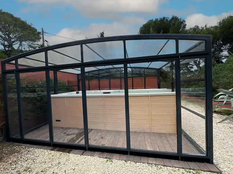 Abri de spa vitré à structure grise dans un jardin
