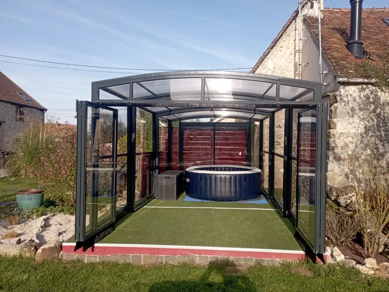 Abri de spa ouvert dans un jardin, à côté d’une maison en pierre