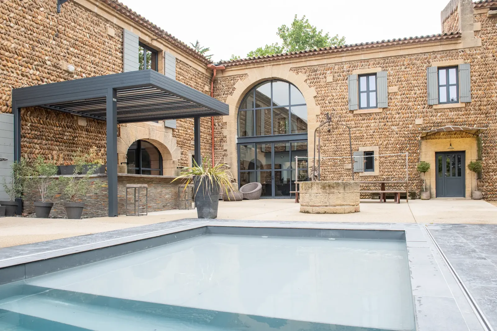 Pergola grise devant une bâtisse en pierre au bord d’une piscine